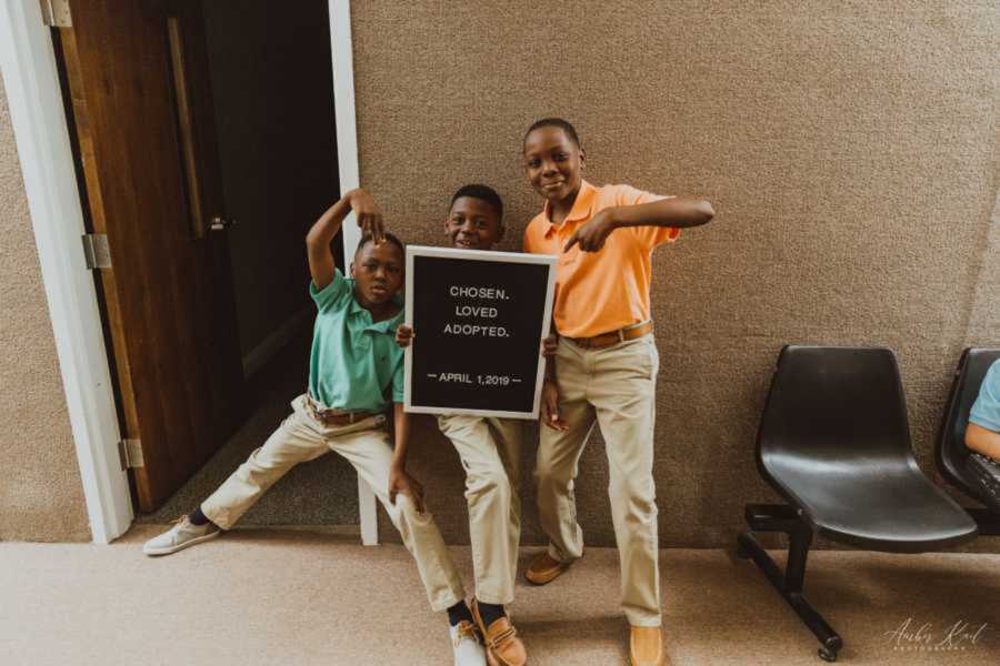 Three adopted siblings posing with letterboard inside court building