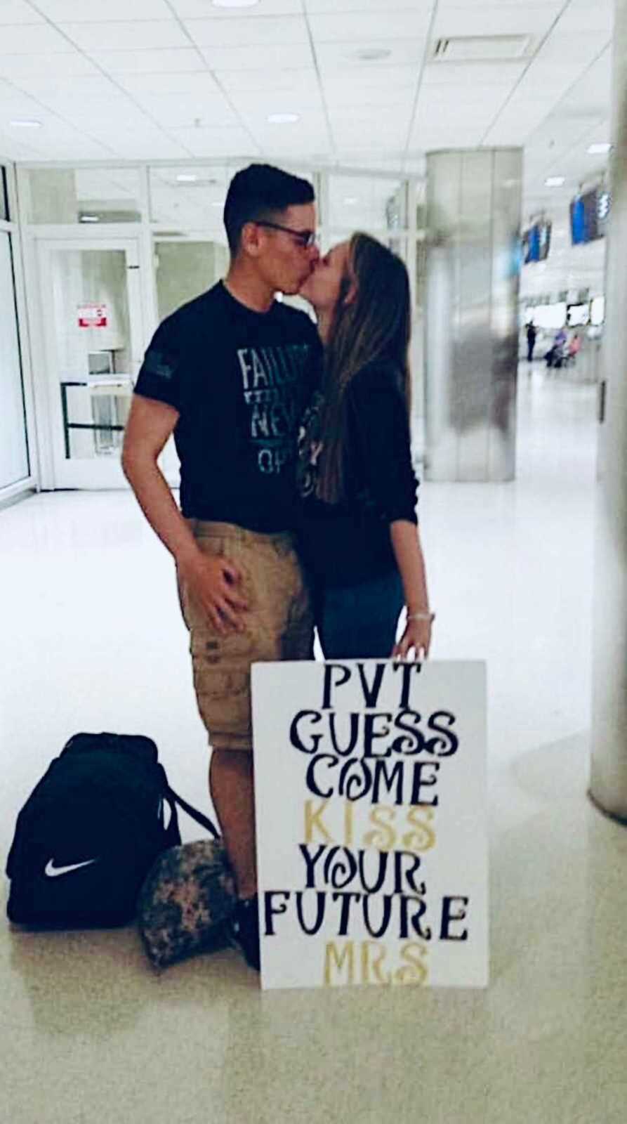 woman kisses army fiance in airport holding sign saying "pvt Guess come kiss your future Mrs."