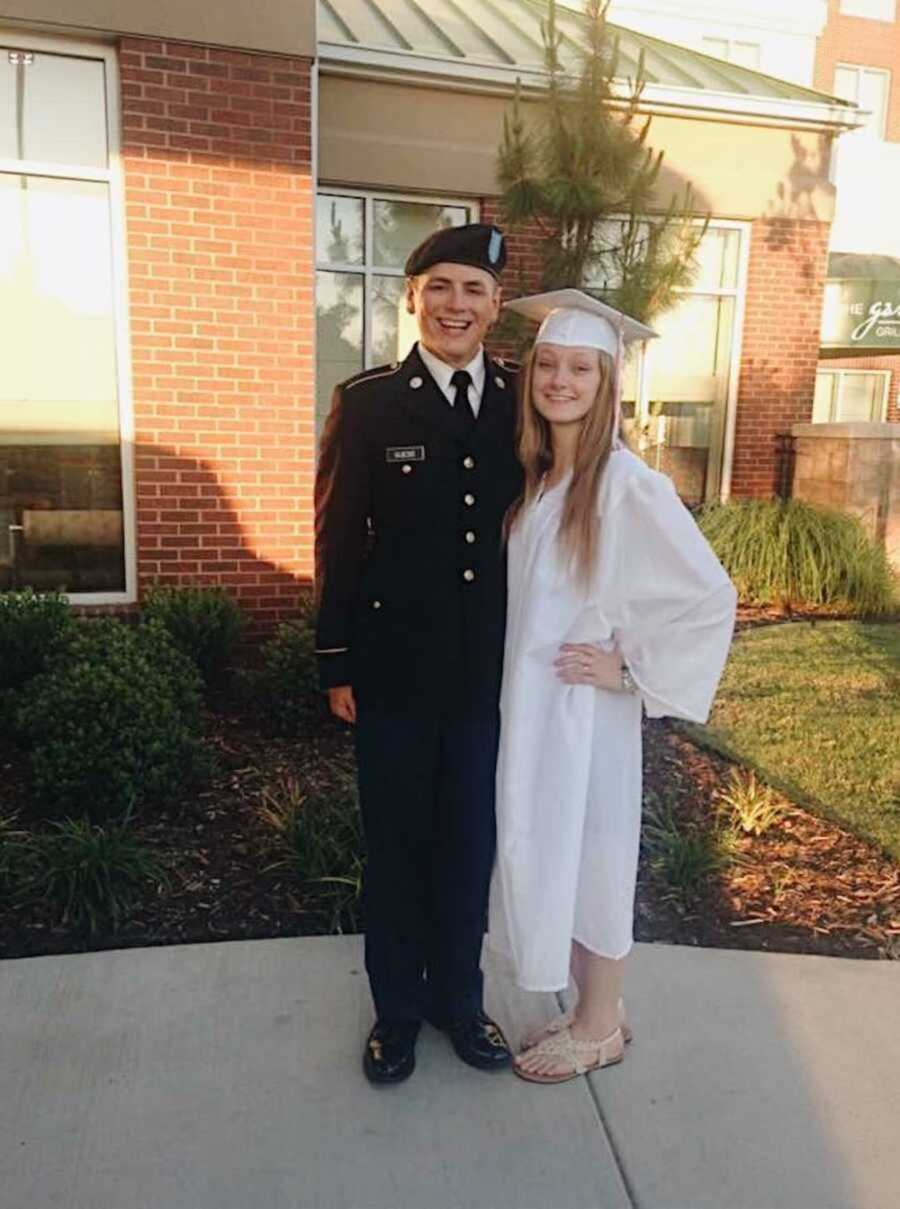 couple stand together in Army uniform and graduation cap and gown
