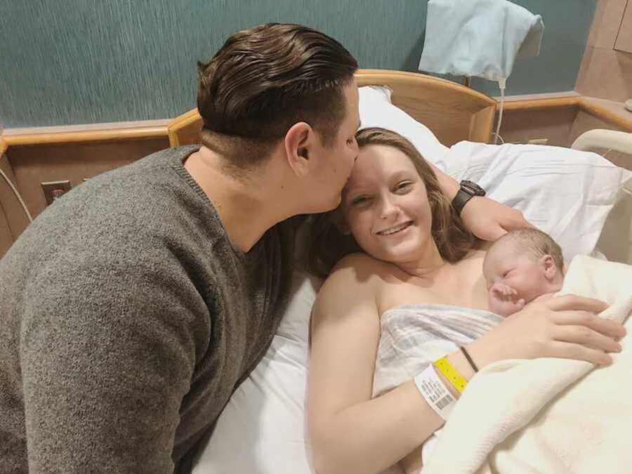 mom holds baby in hospital bed, husband kisses forehead