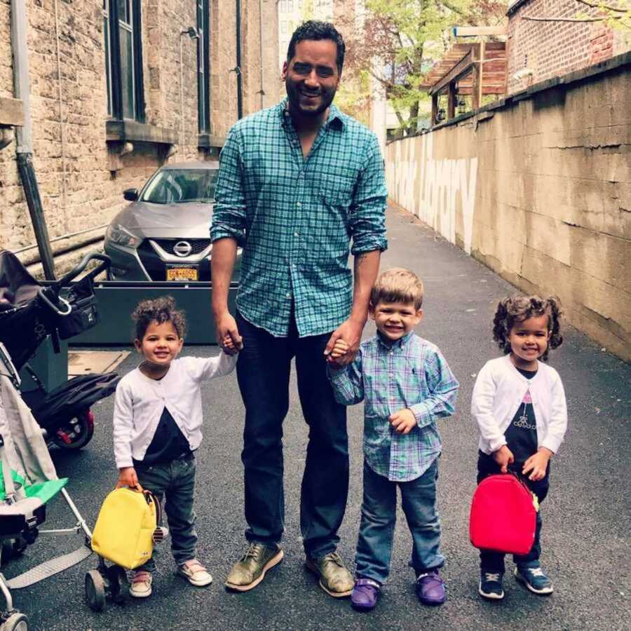 Smiling single dad holding his childrens hands outside