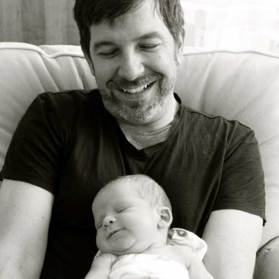 New dad smiling as his newborn son is asleep in his lap