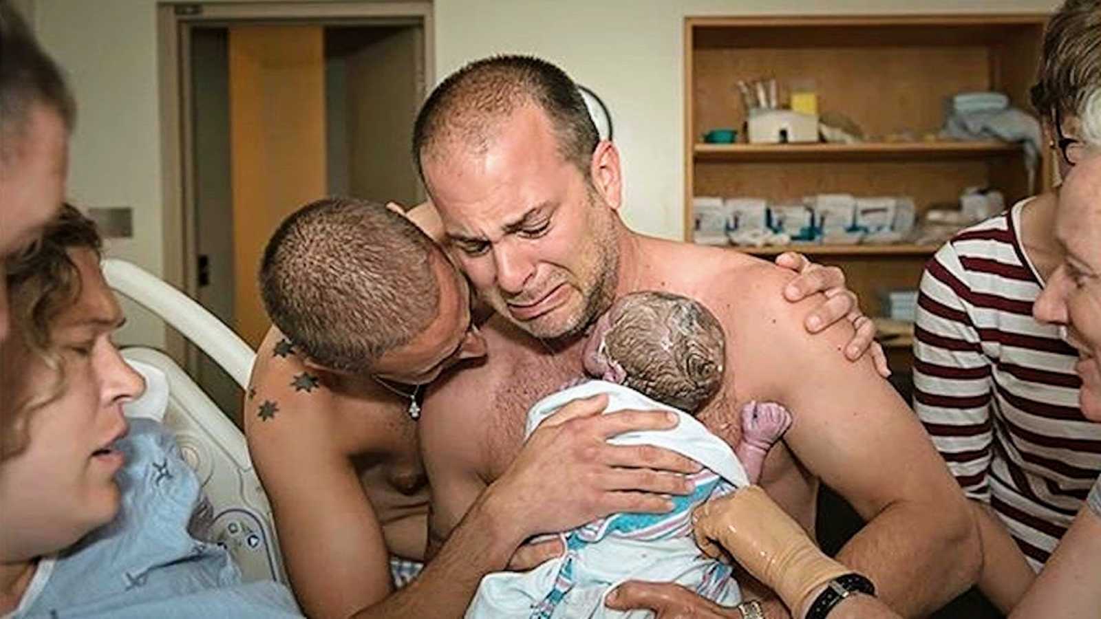 Crying new dads holding their newborn son shirtless in hospital