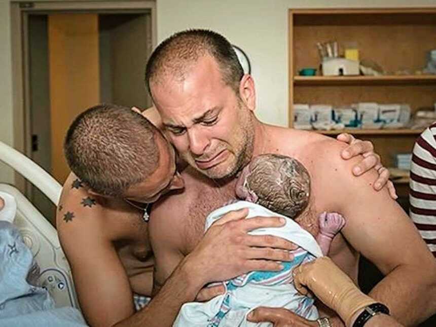 Crying new dads holding their newborn son shirtless in hospital