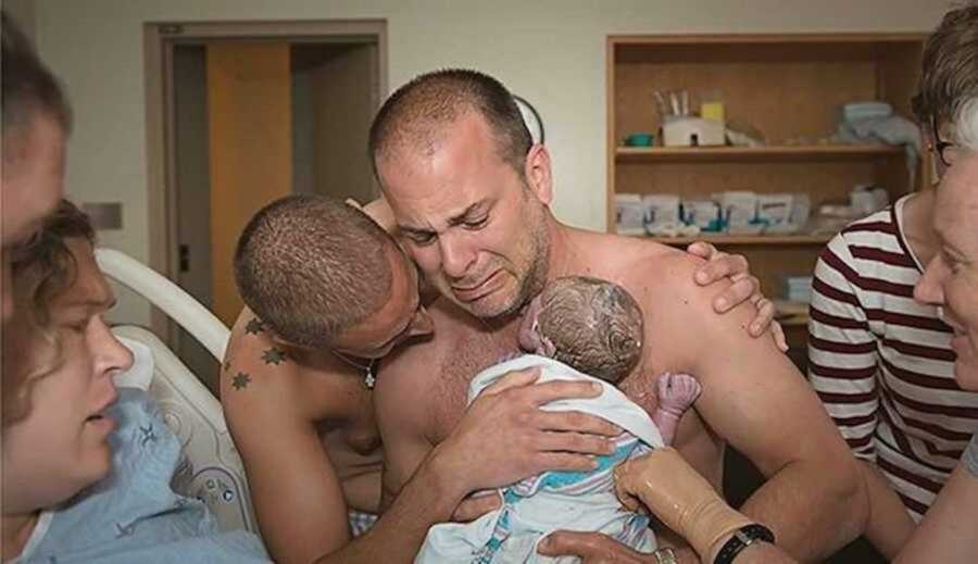 Crying new dads holding their newborn son shirtless in hospital 