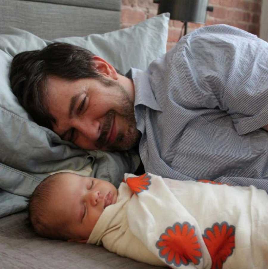 Gay dad smiling down at his sleeping newborn son