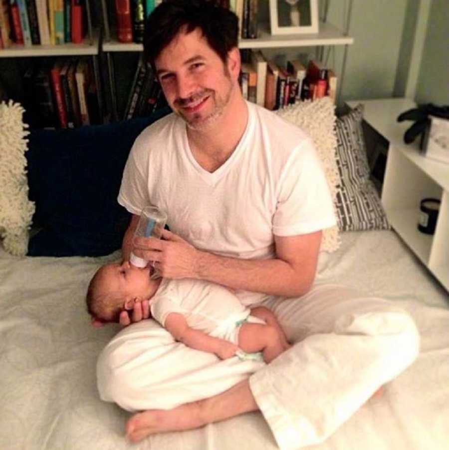 New dad smiling as he feeds his newborn son in bed