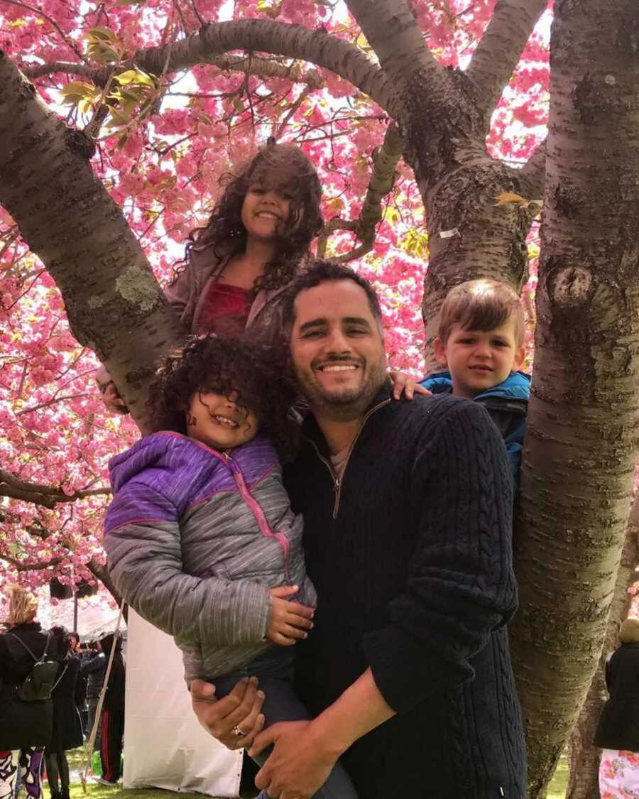Smiling gay dad with his three children in a cherry blossom tree