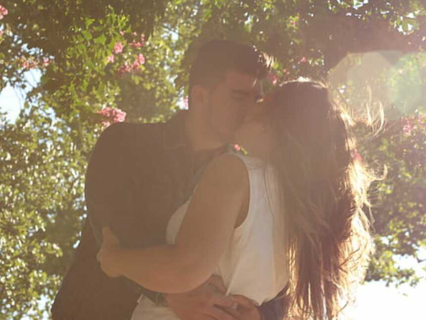 man kisses a woman holding her close under a flowering tree