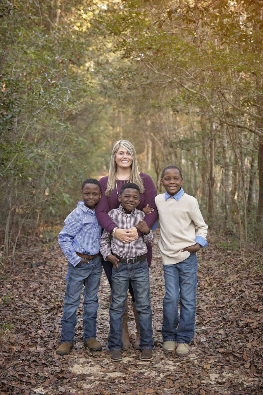 Adoptive mom smiling with three sons in forest 