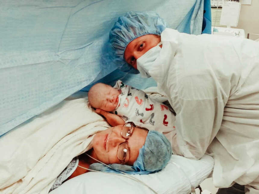 new father holds newborn baby by mother after she gives birth