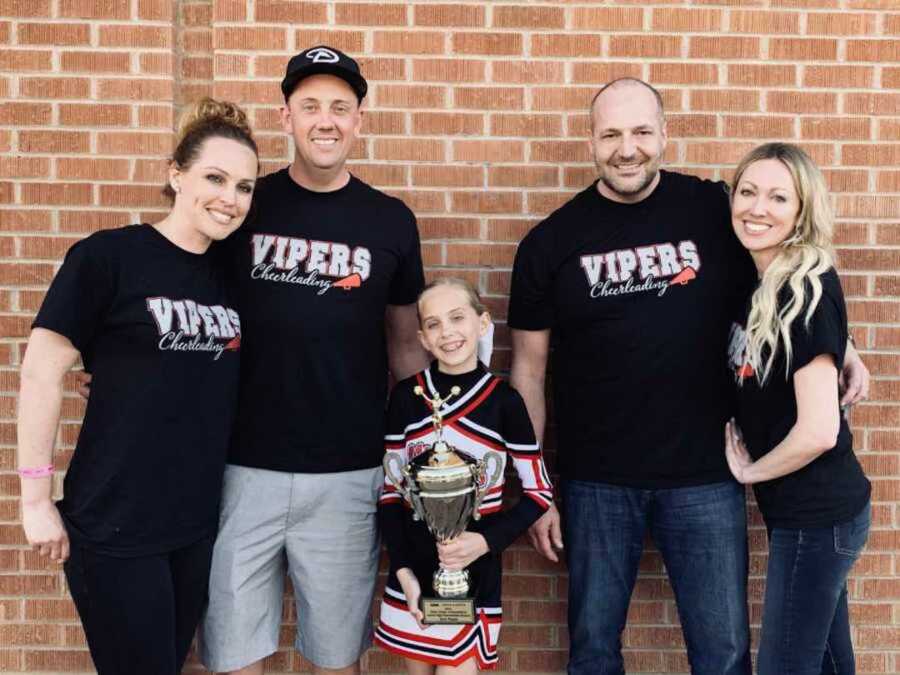 parents smiling with daughter in cheerleader uniform