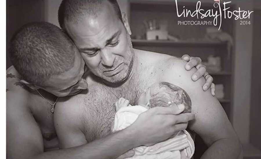 Professional photo of new dads holding their newborn son via surrogacy 