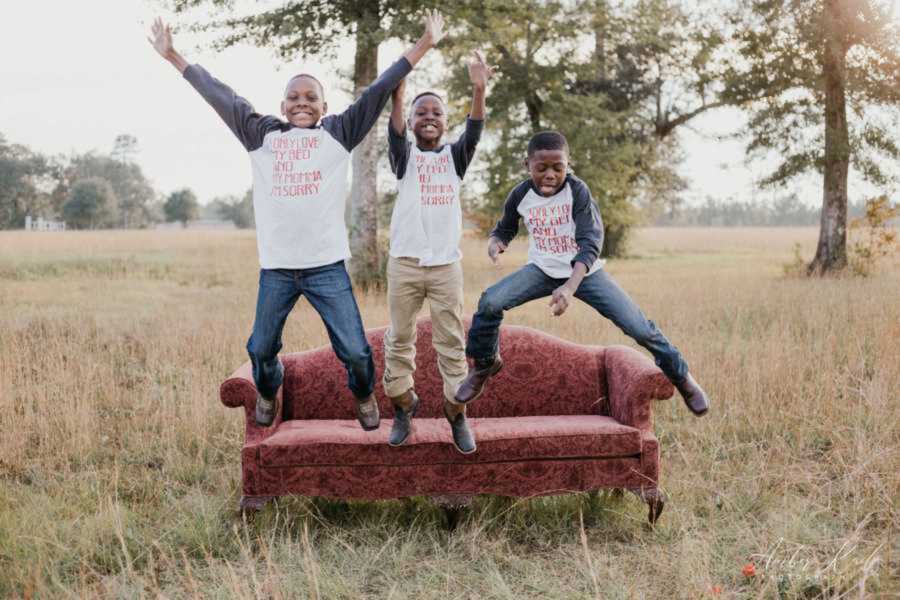 Three brothers jumping off red coach in grassy field