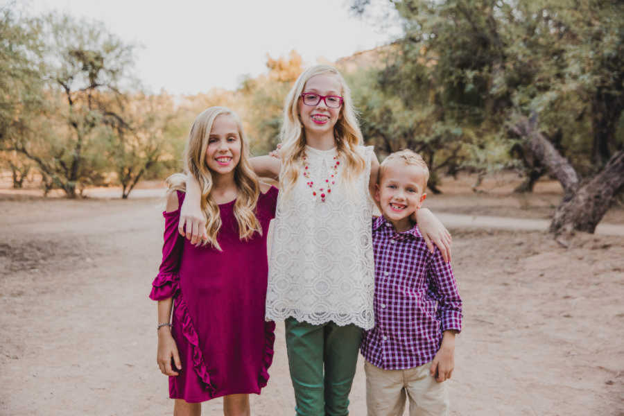 three siblings stand outside with arms around each other