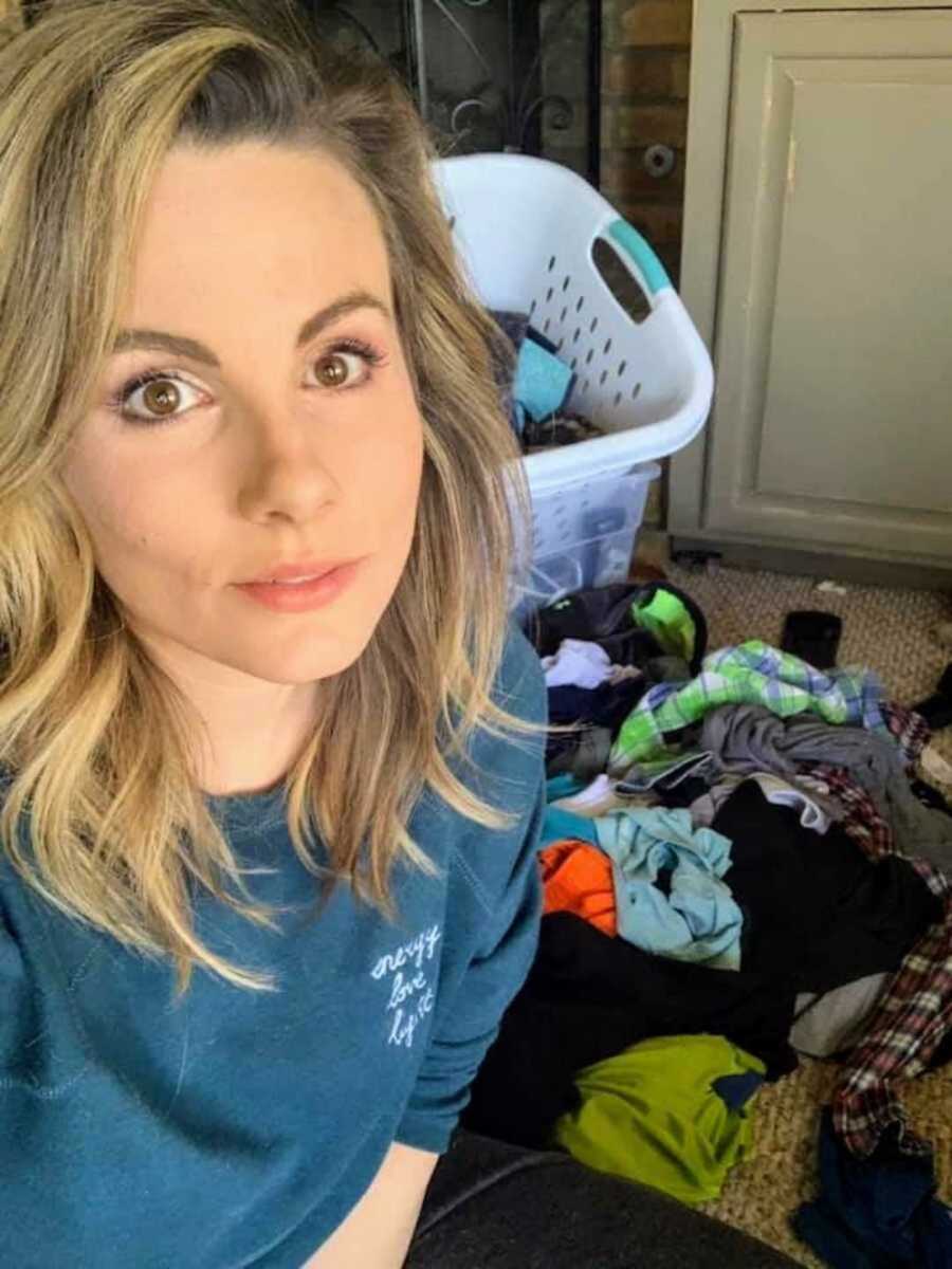 Woman on floor of home amongst pile of clothes and laundry basket