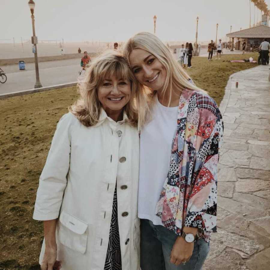 mom and daughter stand next to each other posing by the beach