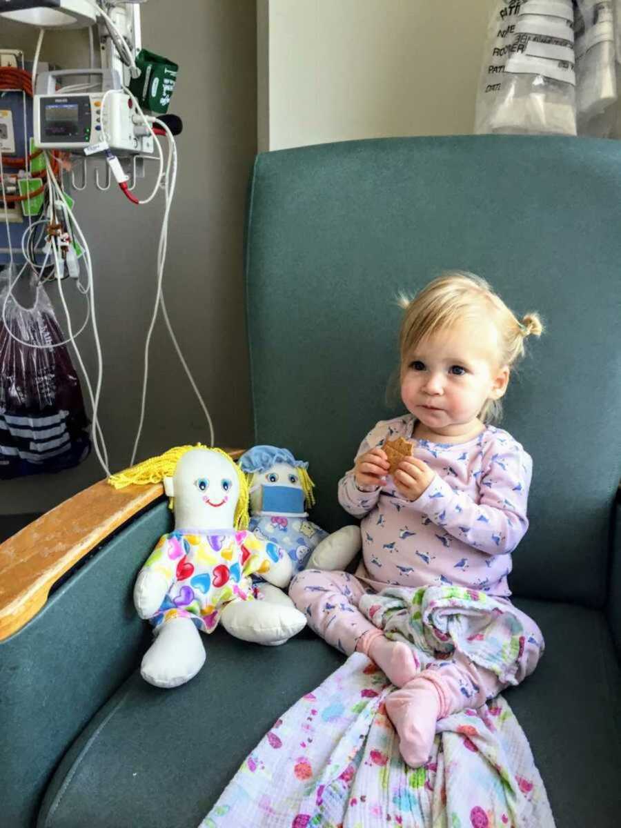 Little girl in pajamas and pigtails munching on a cracker with her toys in hospital chair