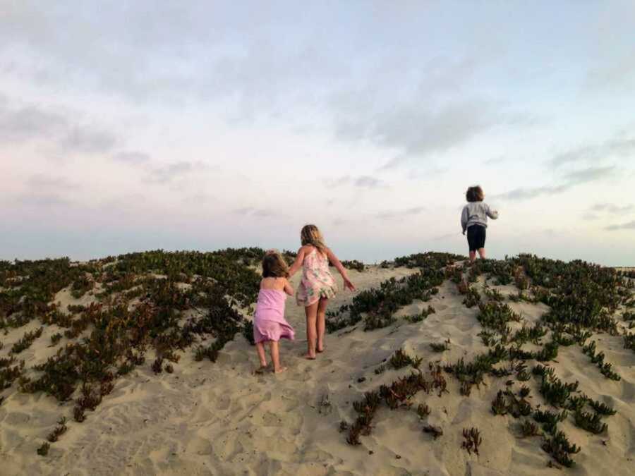 Two little girls and a little boy running up a sandy hill at sunset