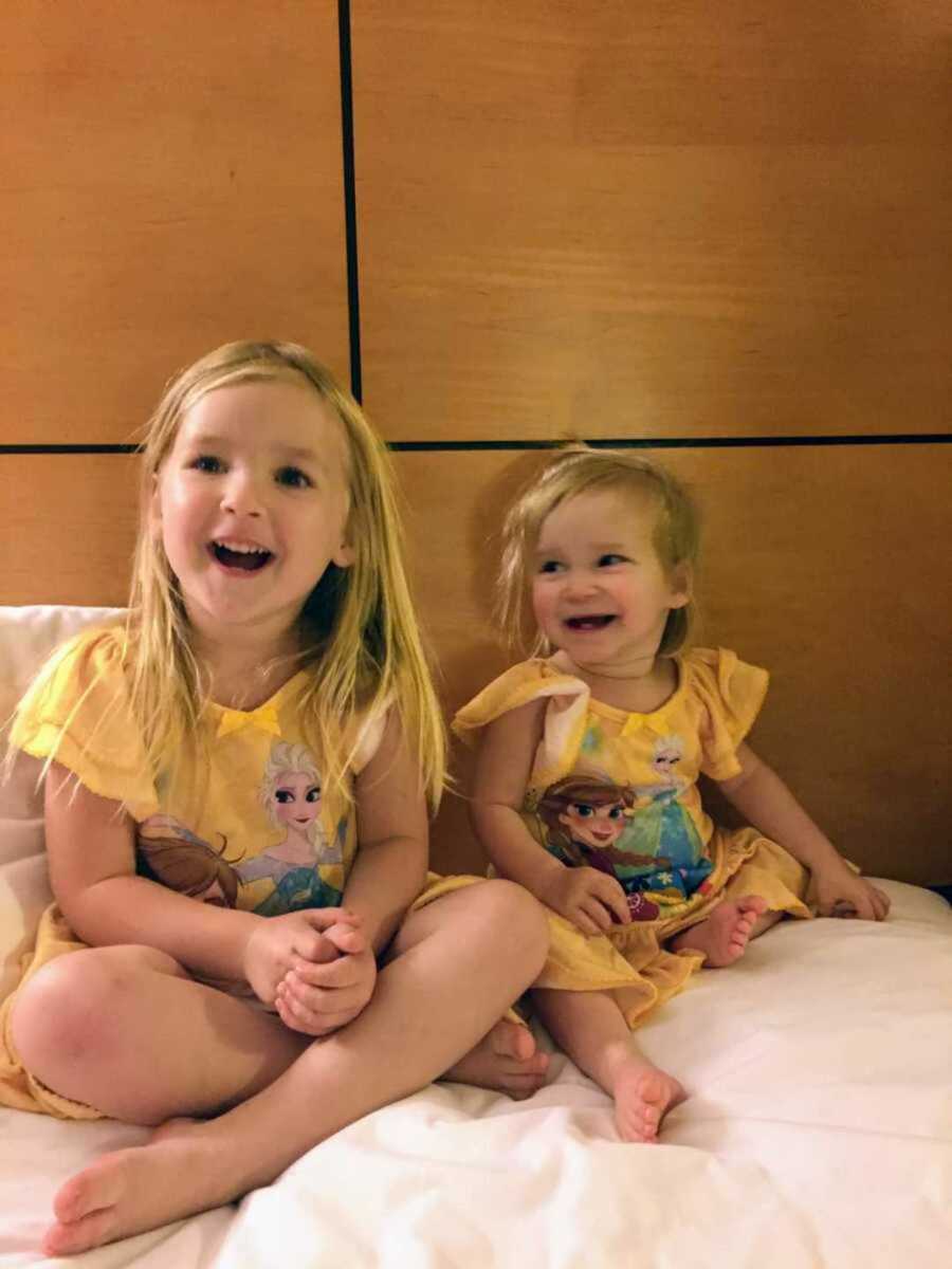 Grinning sisters in matching princess pajamas sitting in bed together