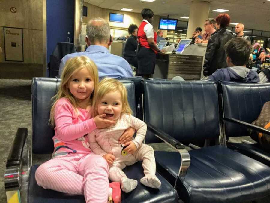 Big sister embracing little sister in a blue chair in the airport