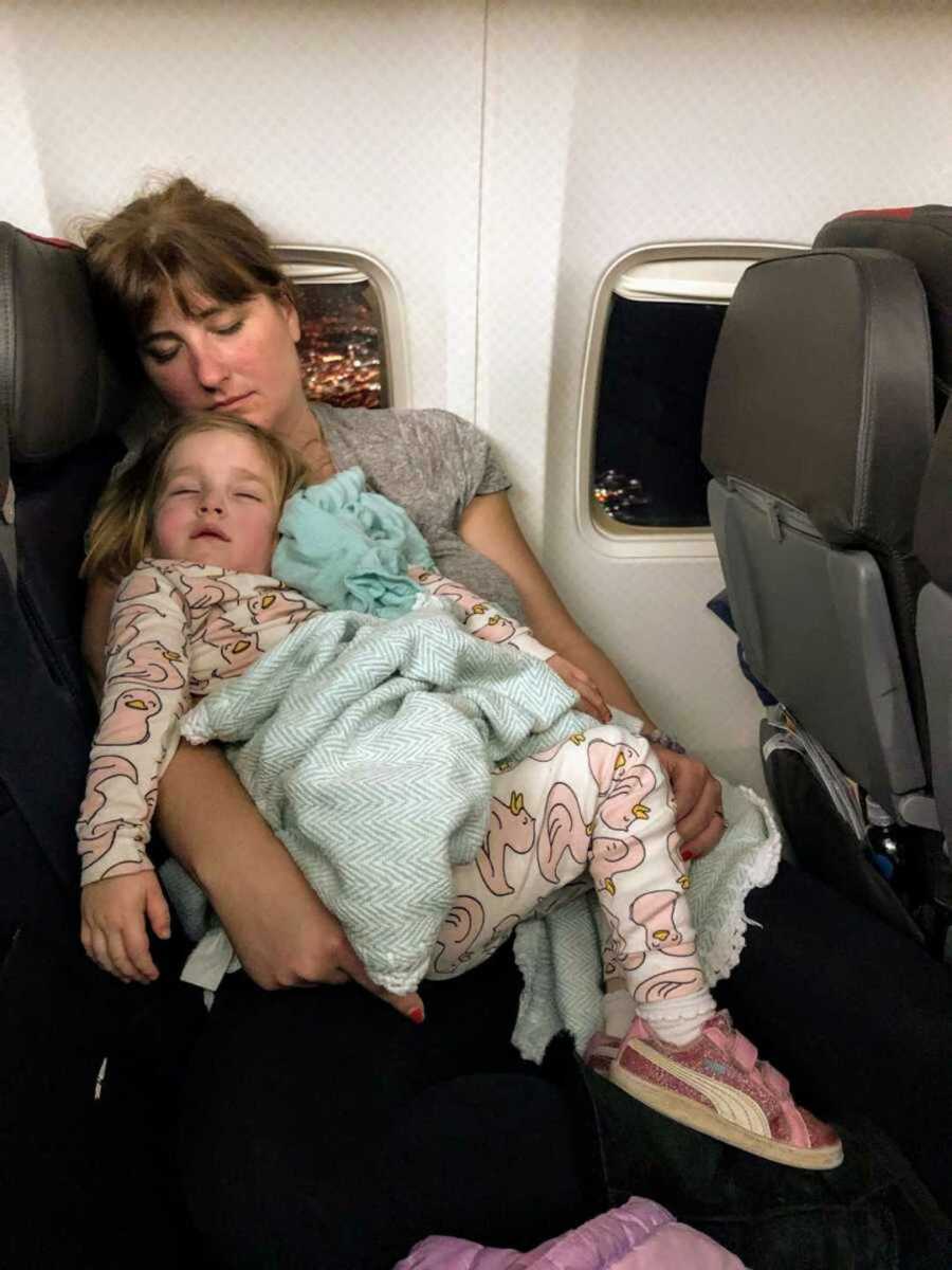 Exhausted mom holding sleeping daughter wearing pajamas in airplane seat