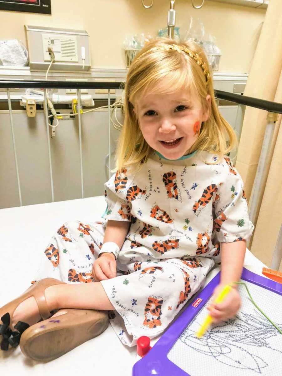 Cheery toddler in a hospital bed and gown playing with toys