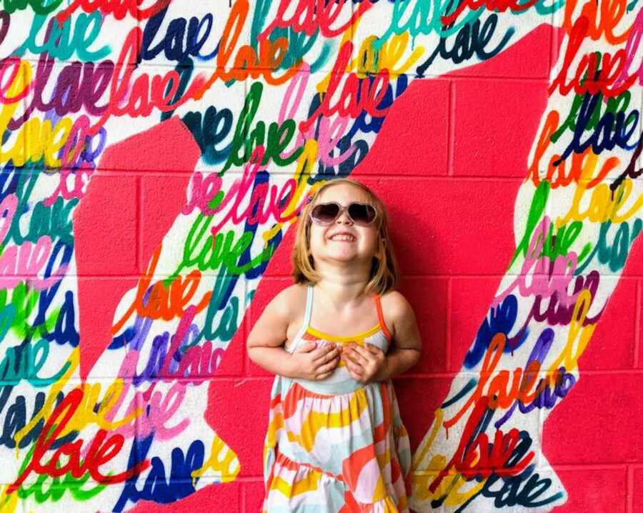 Carefree toddler in bright summer dress standing behind colorful background