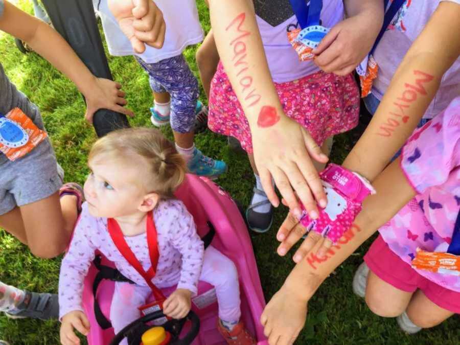 Curious little girl in pink toy car surrounded by children