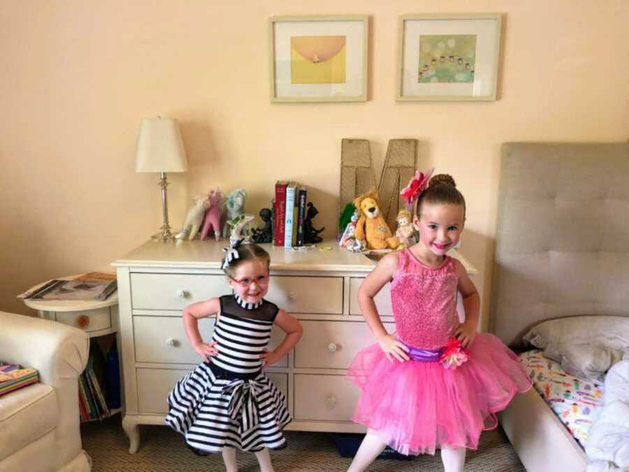 Grinning sisters in bedroom with frilly outfits on and smiling with hands on hips 