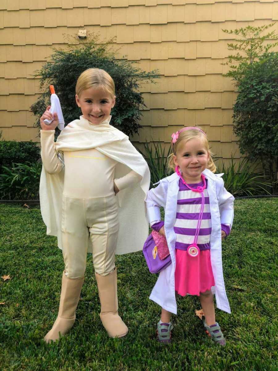 Two smiling little girls in green backyard in halloween costumes