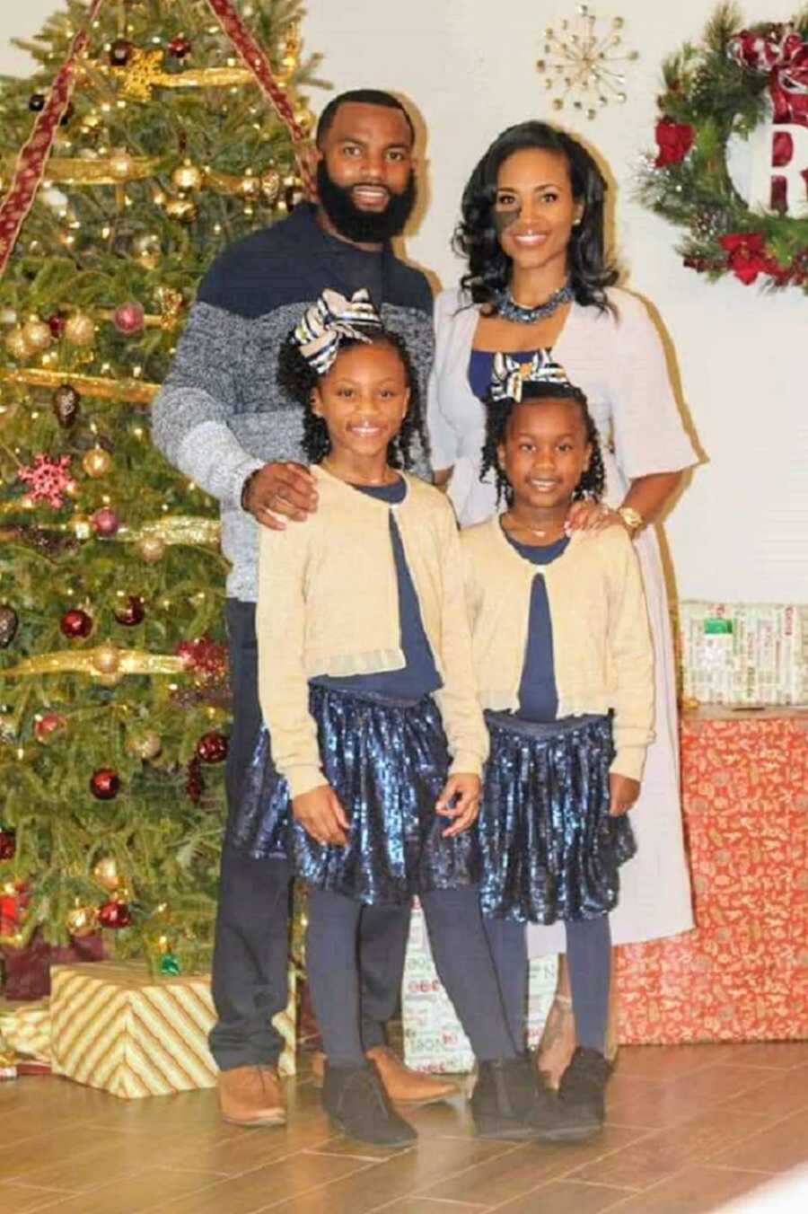 Family of four standing in front of Christmas tree