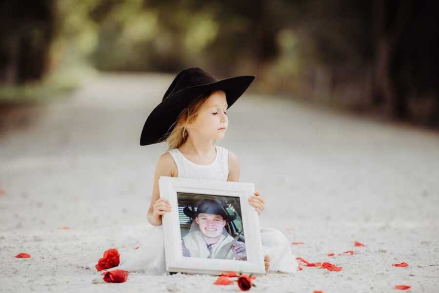 young girl holds photo of newly-deceased dad while wearing his hat