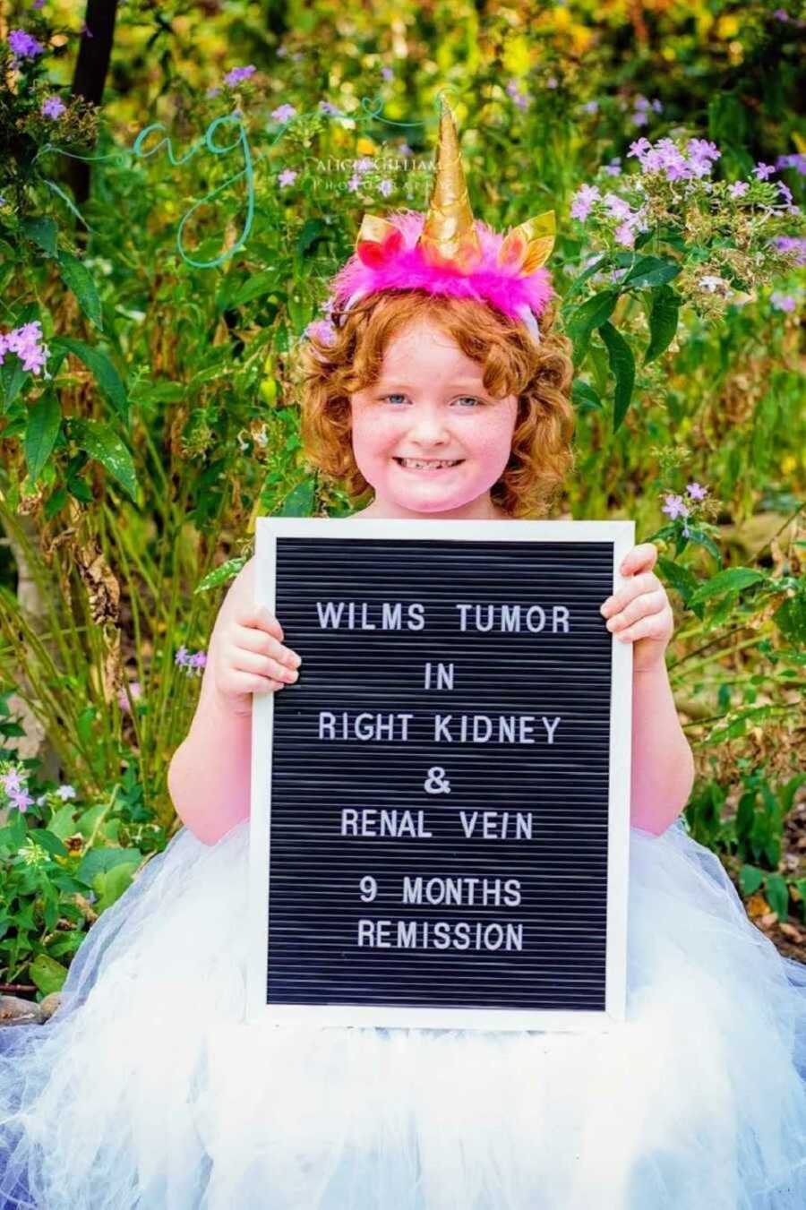 girls stands with sign that signs "wilms tumor in right kidney & renal vein. 9 months remission"