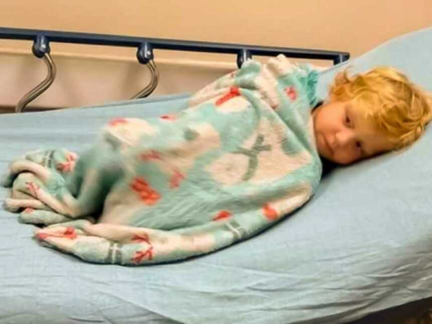 Blonde boy lying in hospital bed under blanket