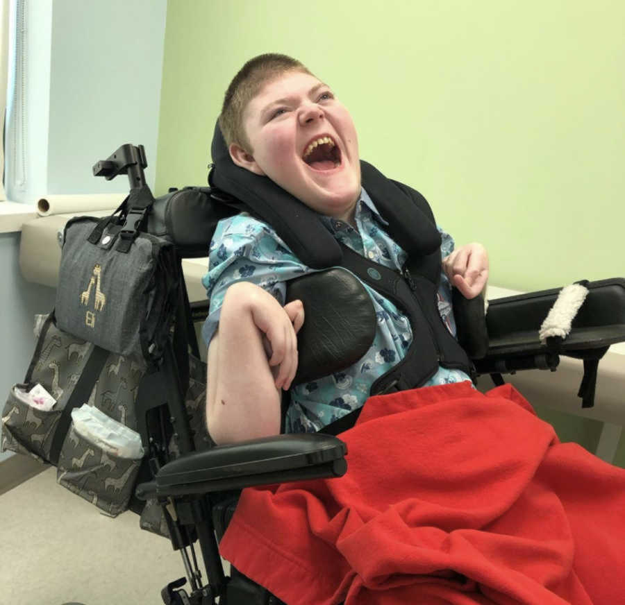 Happy disabled child sitting in his chair with a red blanket over him