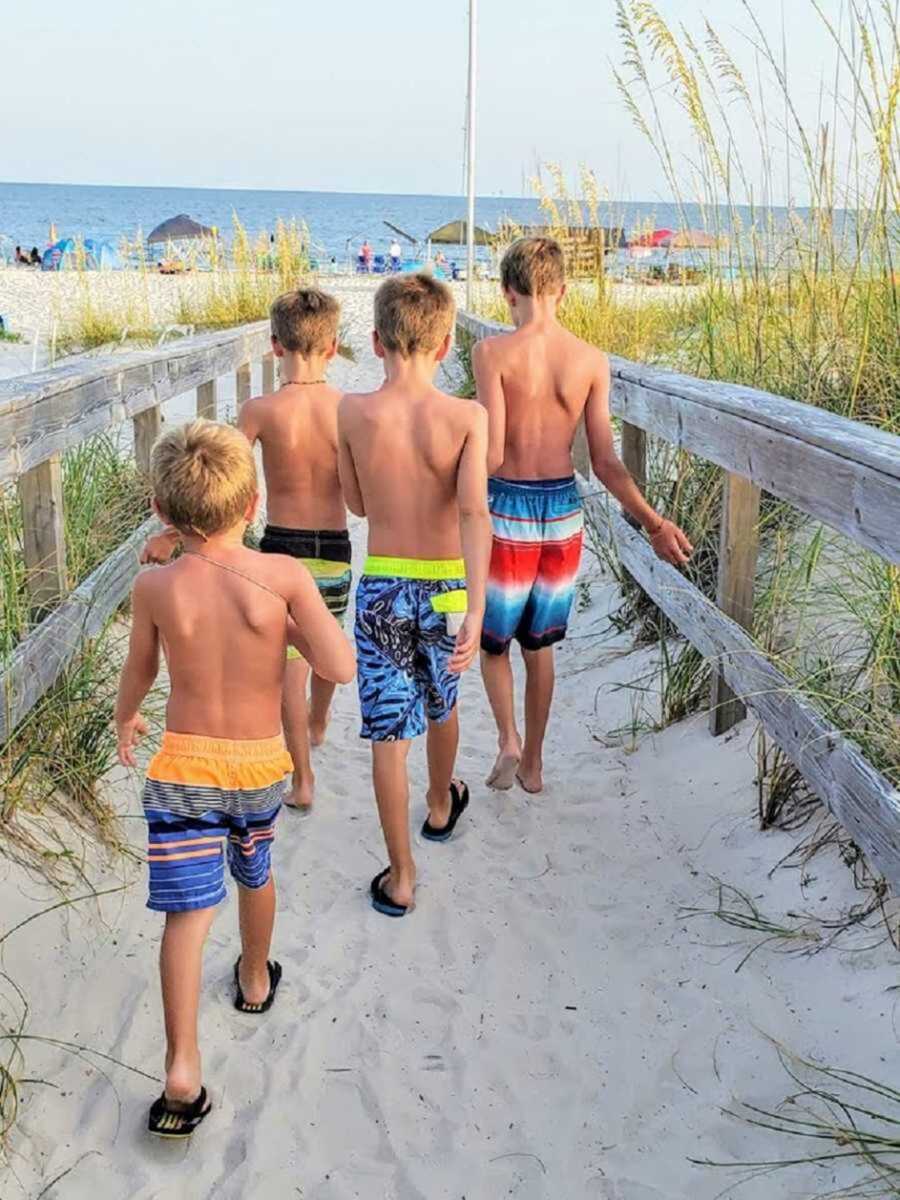 four brothers walk in sand towards the beach