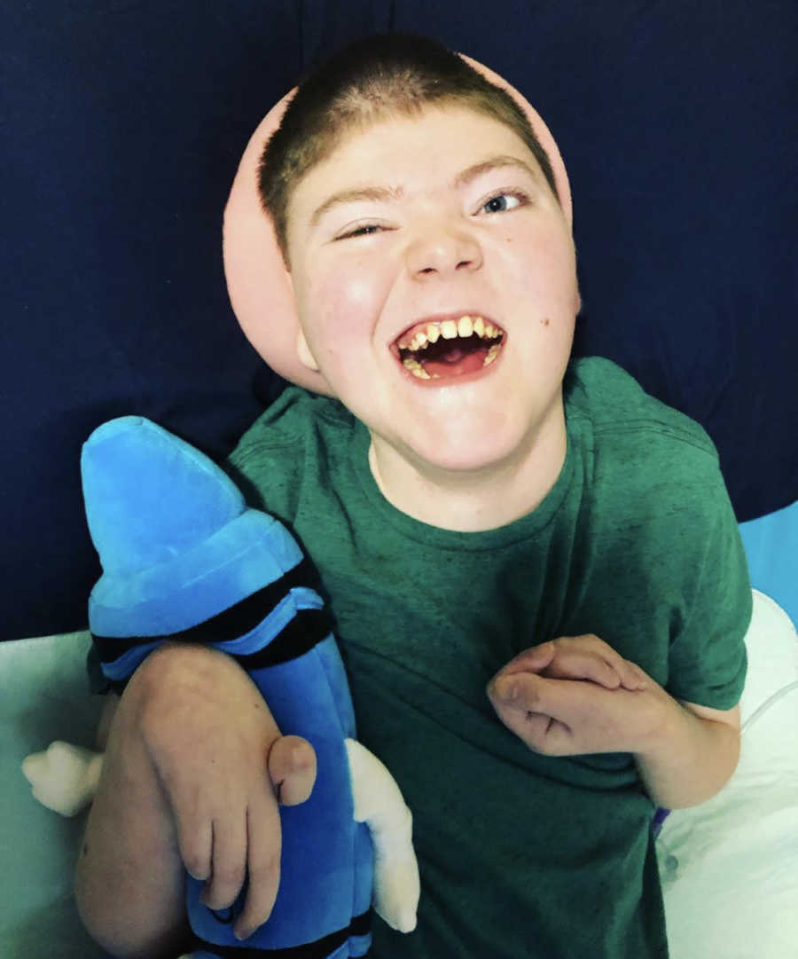 Joyous disabled child with green shirt on gripping a blue stuffed crayon