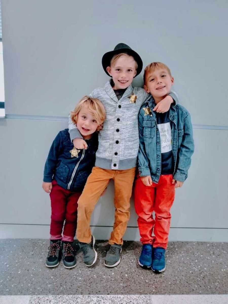 three young children stand together in front of grey wall