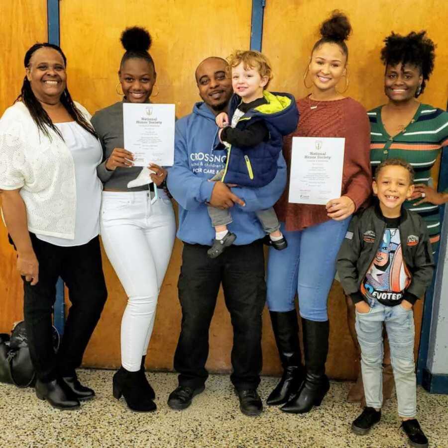 Adoptive family smiling in classroom holding honor society awards