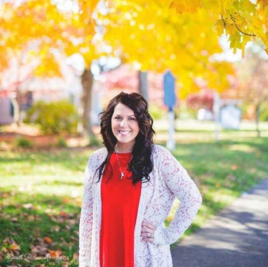 birth mom wears white cardigan and red shirt posing in fall foliage