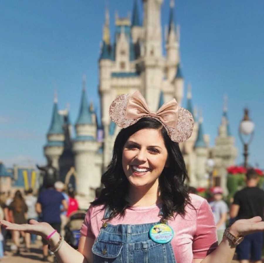 birth mom poses with hands out in front of Cinderella's castle