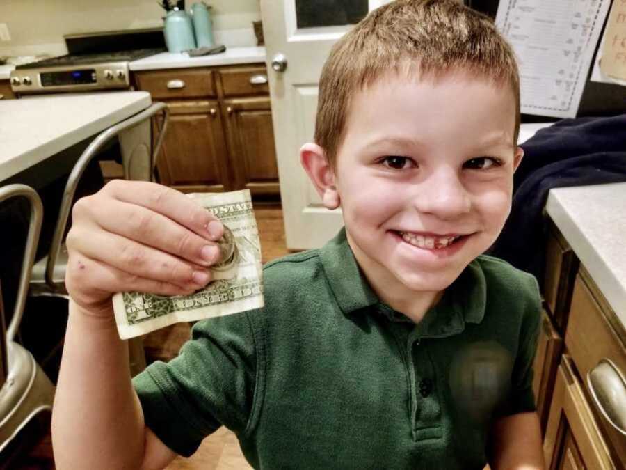 Young boy wearing a green shirt holds up a dollar bill while smiling