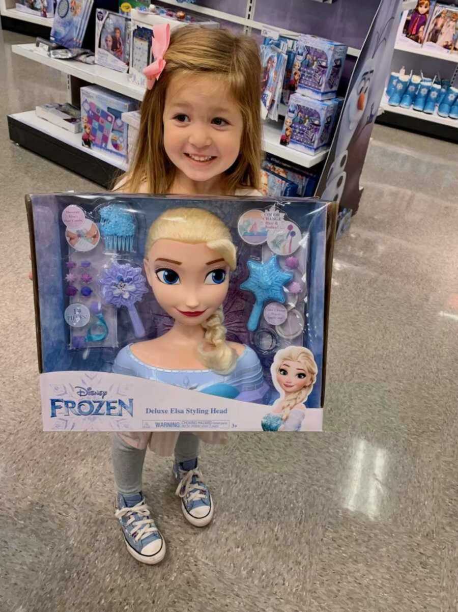 girl smiles while holding Elsa toy in store