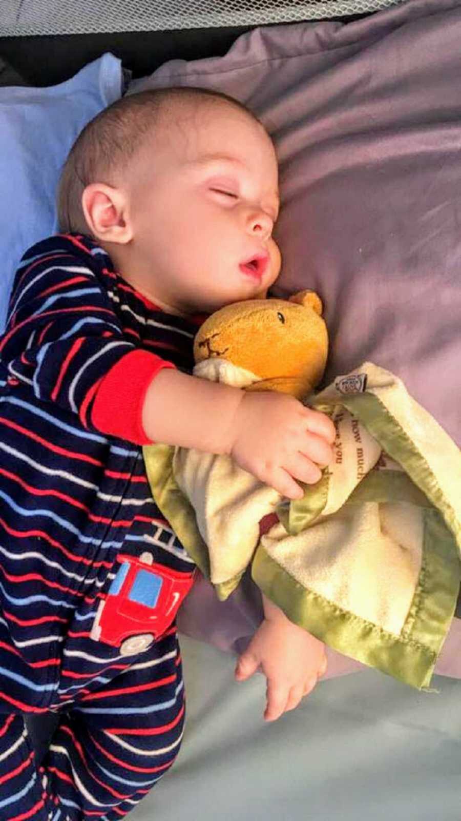infant boy laying in bed holding a stuffed animal