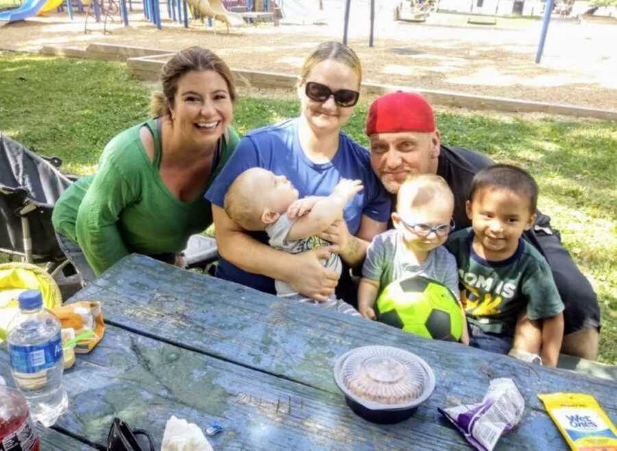 Smiling foster mom with little boys biological parents sitting at picnic bench