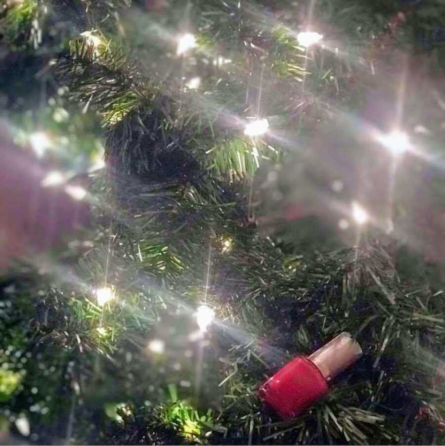 Red nail polish sitting in a Christmas tree with lights