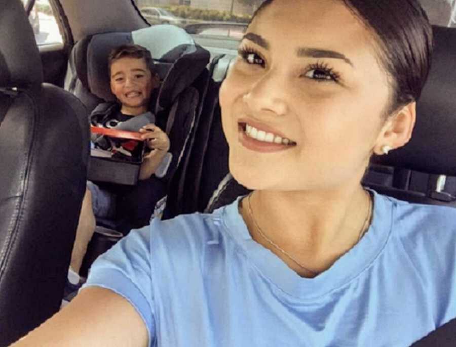 Mom in blue t shirt smiling next to son car seat