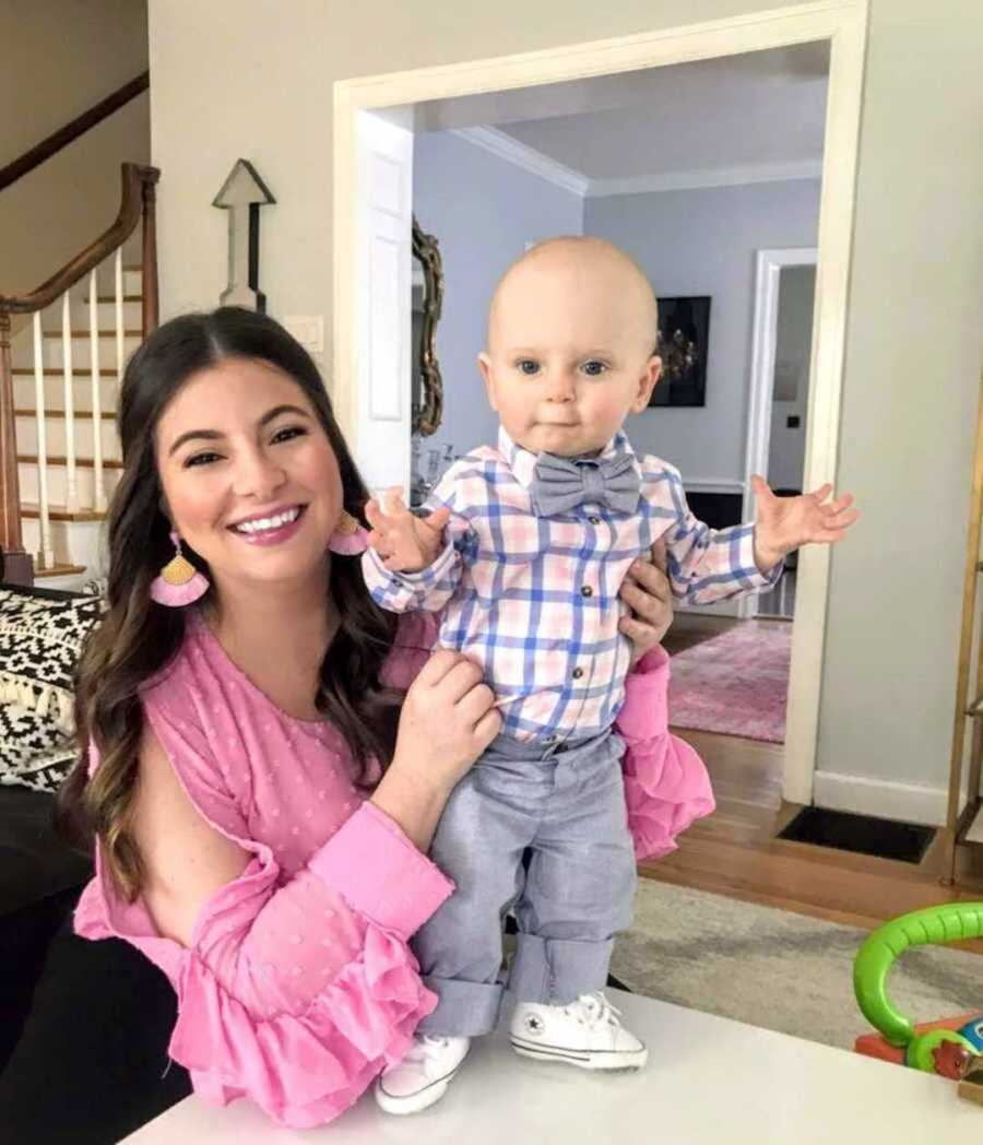 Joyous foster mom in pink holding up baby boy in bowtie and converse