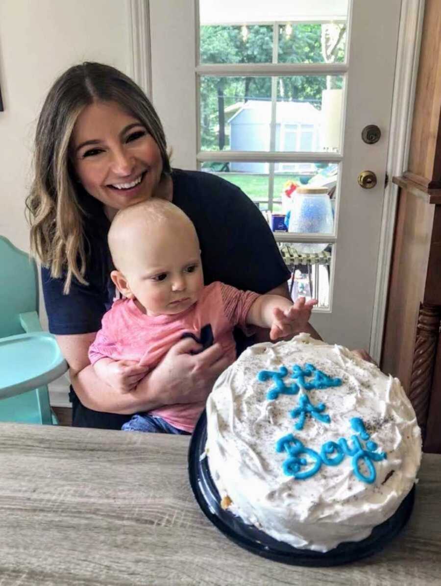 Proud foster mom holding adopted little boy in front of white and blue cake 